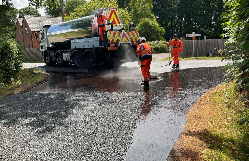 Workers in orange high vis spreading bitumen on the road from a lorry