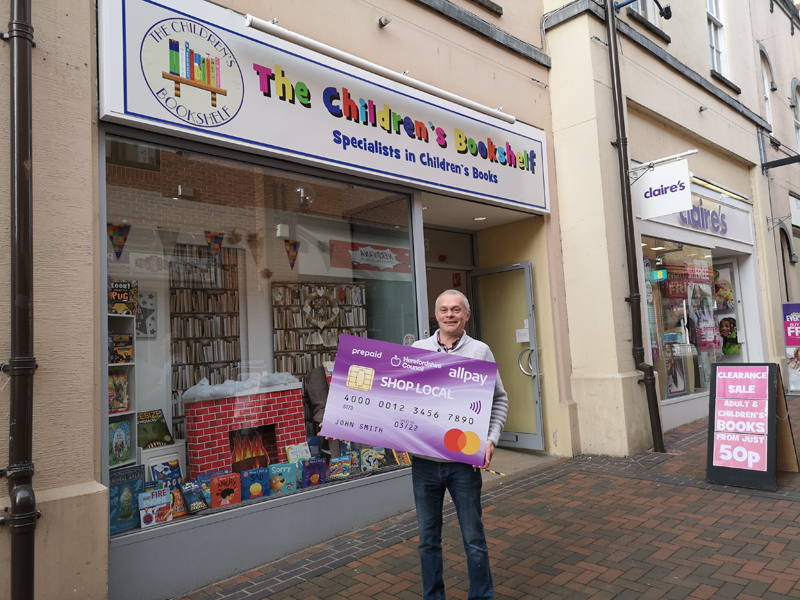 Owner of Childrens Bookshelf outside shop with Shop Local card