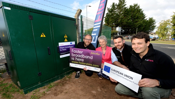 Councillor Trish Marsh and George Thomas, Director at G. P. Thomas Construction with Dan Jones and Oliver Helm from Full Fibre Limited crouched down next to a telephone exchange