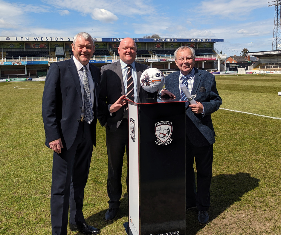 Paul Walker, Chief Executive Herefordshire Council, Chris Ammonds, Chairman Hereford FC Chairman and Councillor Harry Bramer at Edgar Street Stadium in front of match ball April 20 2024