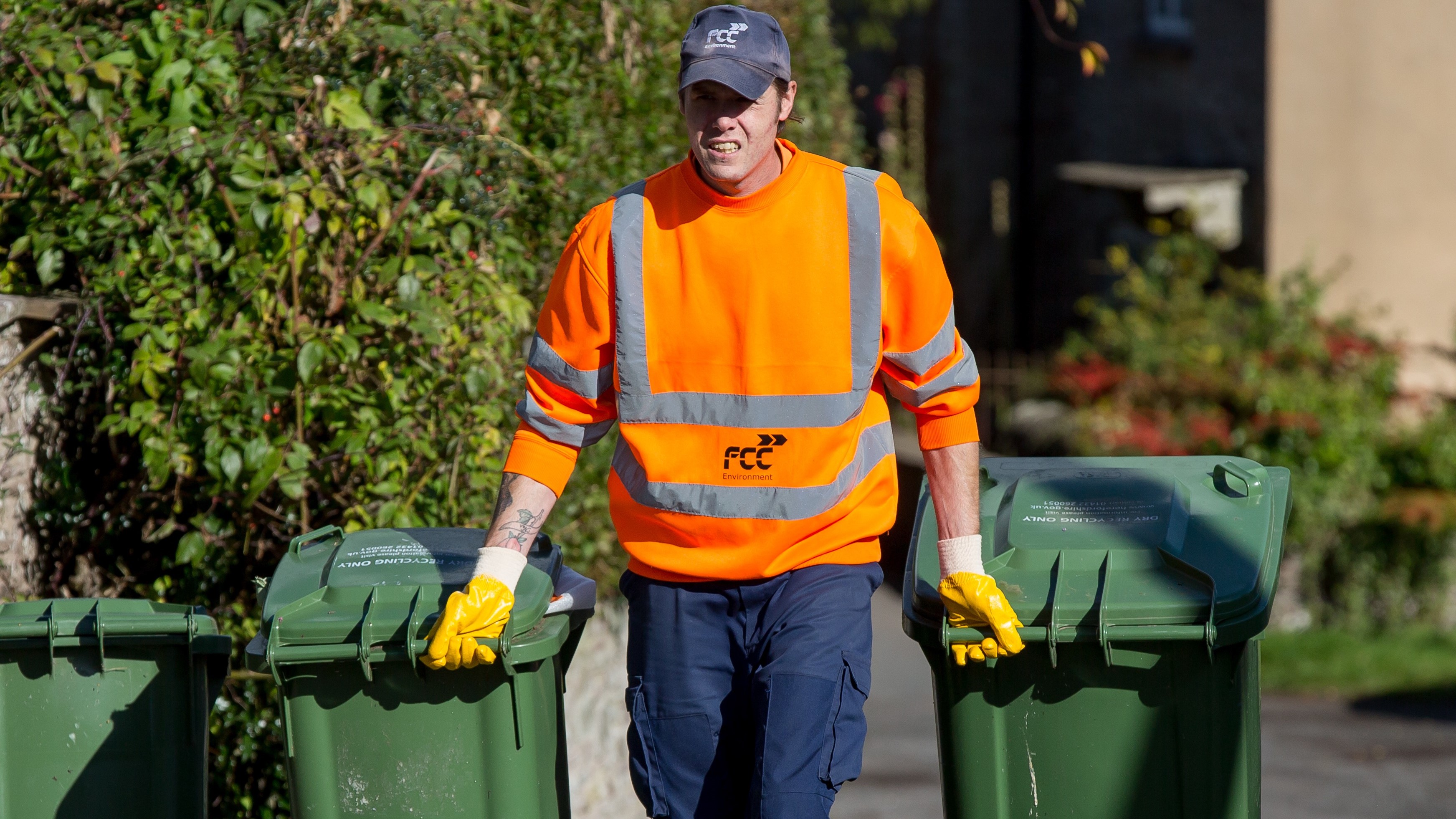 Waste team member pulls two green wheelie bins