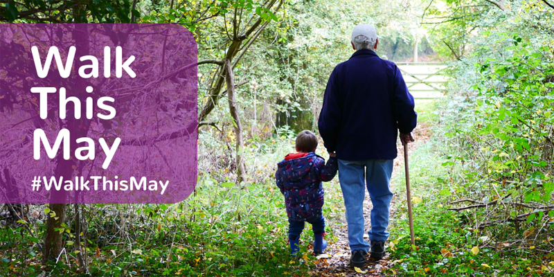 Older man and young child taking a walk in woodland, with sun coming through trees