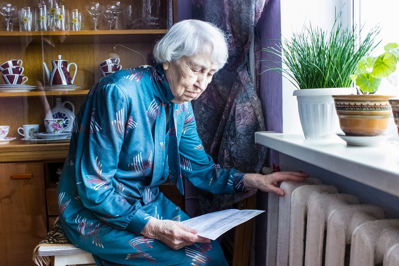 Senior citizen touching radiator and reading letter